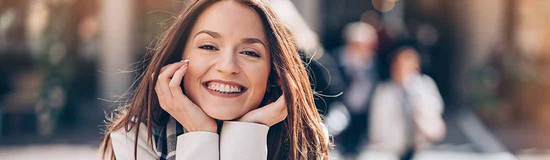 Dentist Orlando FL Teenager With Retainer Outside City photo of a teenage girl with braces smiling with her hands on her chin holding her head